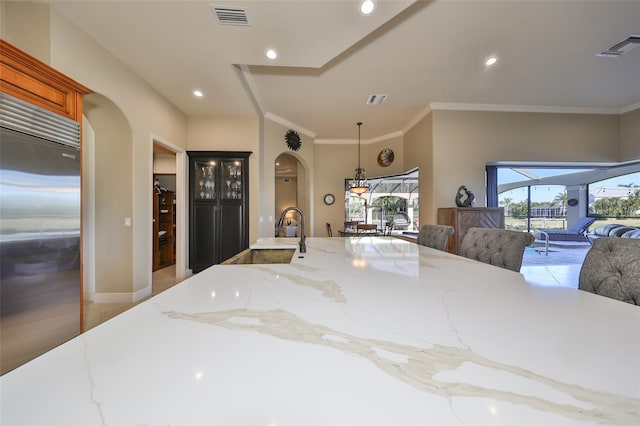 kitchen with light tile patterned flooring, built in fridge, ornamental molding, light stone counters, and sink