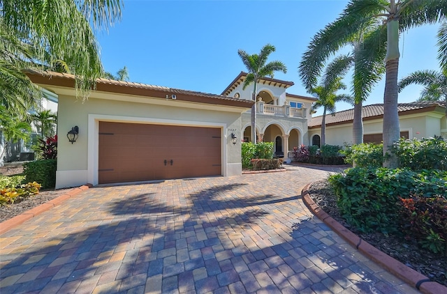 mediterranean / spanish house with a garage, decorative driveway, a balcony, and stucco siding