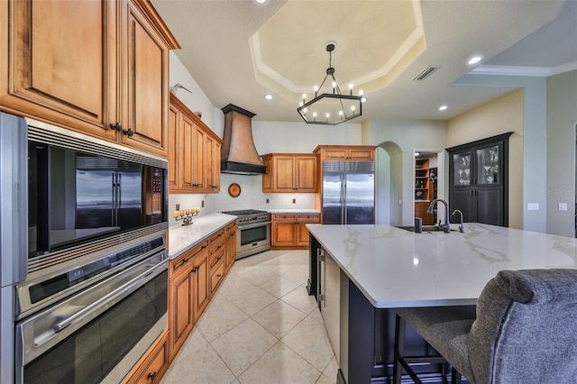 kitchen featuring built in appliances, arched walkways, a sink, custom exhaust hood, and a tray ceiling