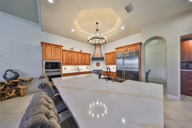 kitchen featuring custom exhaust hood, a raised ceiling, visible vents, a sink, and built in appliances