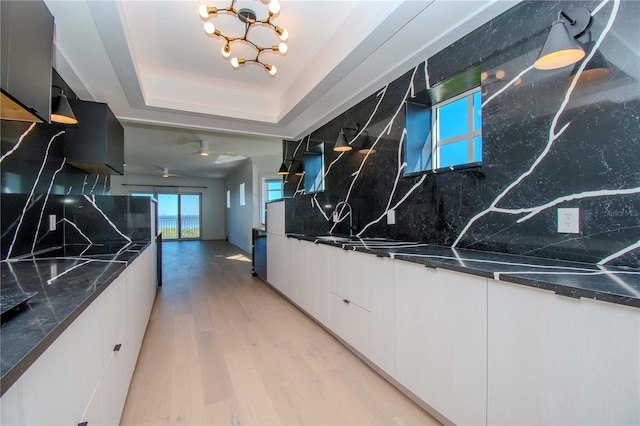 kitchen with an inviting chandelier, backsplash, dark stone countertops, light hardwood / wood-style floors, and white cabinets