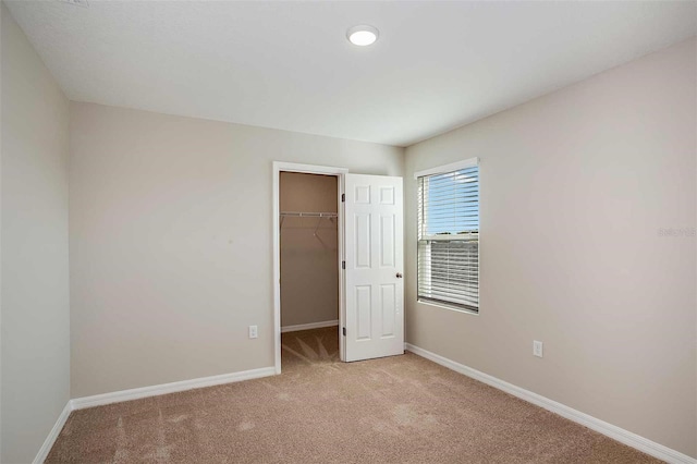 unfurnished bedroom featuring a walk in closet, light colored carpet, and a closet