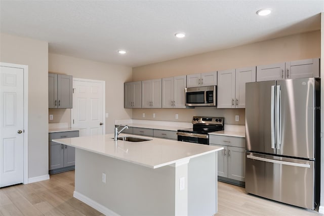 kitchen featuring gray cabinetry, sink, an island with sink, appliances with stainless steel finishes, and light hardwood / wood-style floors