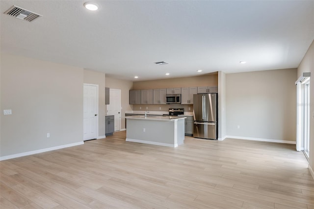 kitchen featuring gray cabinetry, a center island with sink, stainless steel appliances, and light hardwood / wood-style flooring