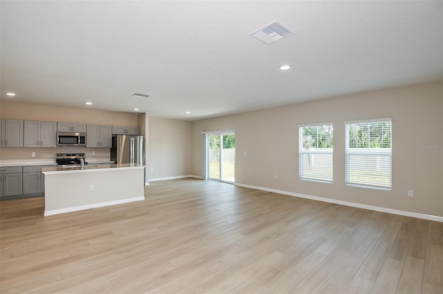 kitchen with gray cabinets, a kitchen island with sink, stainless steel appliances, and light wood-type flooring