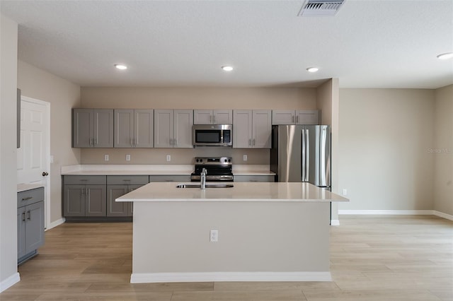 kitchen with a center island with sink, light hardwood / wood-style floors, gray cabinets, and appliances with stainless steel finishes