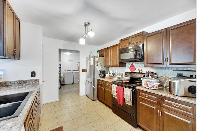 kitchen with decorative backsplash, light stone counters, black appliances, washer and dryer, and hanging light fixtures