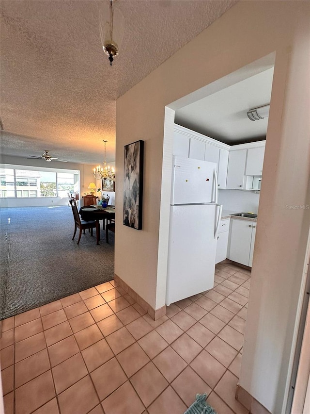 kitchen featuring white cabinetry, white refrigerator, a textured ceiling, light carpet, and ceiling fan with notable chandelier