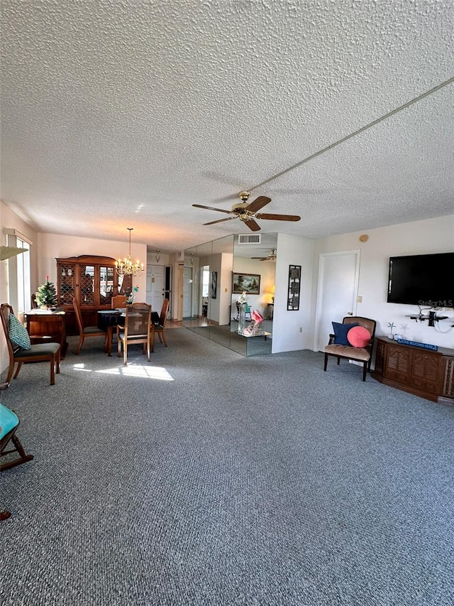 living room featuring ceiling fan with notable chandelier, carpet floors, and a textured ceiling