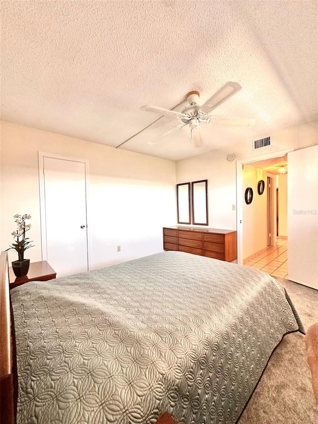 bedroom with ceiling fan, light carpet, and a textured ceiling