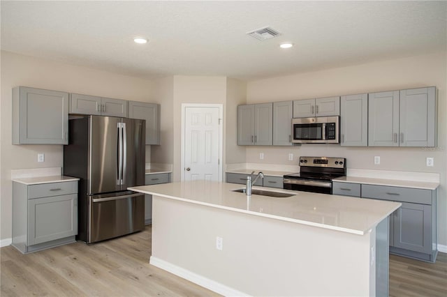 kitchen featuring sink, gray cabinets, an island with sink, appliances with stainless steel finishes, and light hardwood / wood-style floors