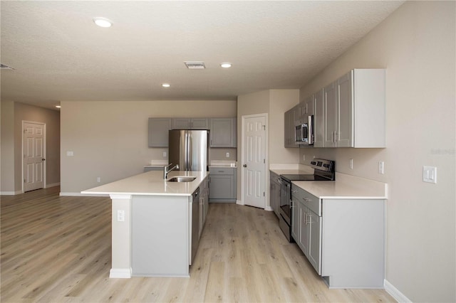 kitchen featuring appliances with stainless steel finishes, gray cabinetry, a textured ceiling, a kitchen island with sink, and light hardwood / wood-style flooring