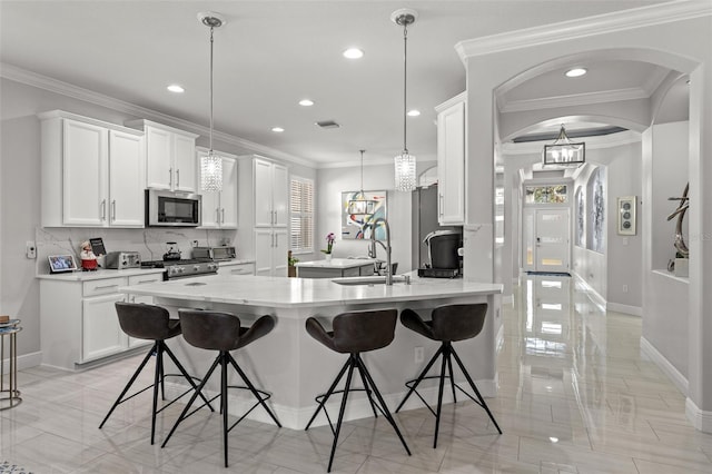 kitchen with a kitchen island with sink, ornamental molding, appliances with stainless steel finishes, decorative light fixtures, and white cabinetry