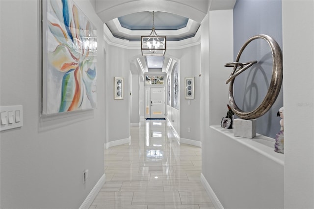 hallway featuring a raised ceiling, ornamental molding, and a chandelier