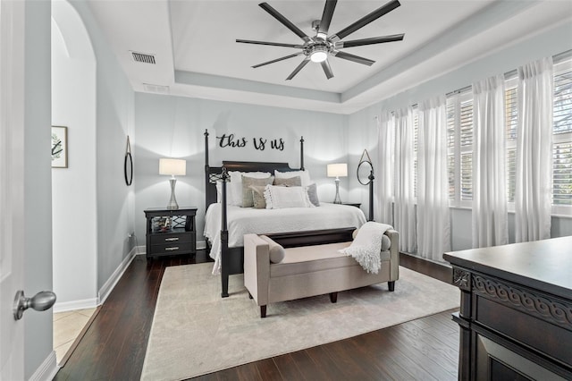 bedroom with ceiling fan, dark wood-type flooring, and a tray ceiling