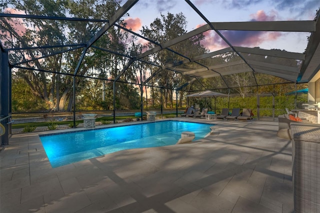 pool at dusk featuring glass enclosure and a patio area