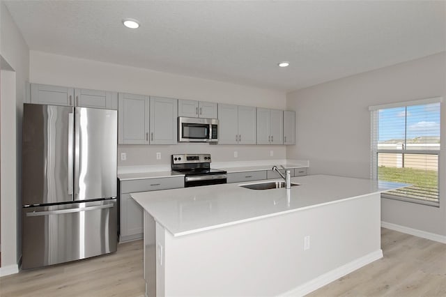 kitchen featuring sink, stainless steel appliances, a center island with sink, and light wood-type flooring