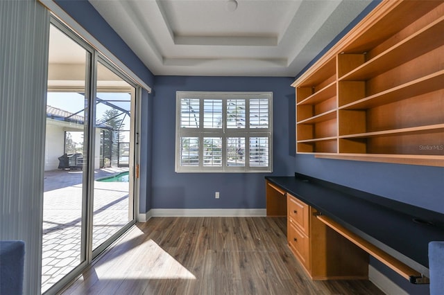 unfurnished office featuring a raised ceiling, dark hardwood / wood-style flooring, and built in desk