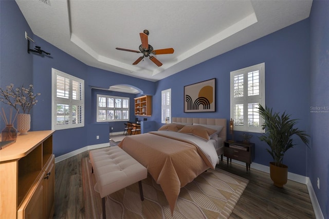 bedroom with ceiling fan, dark hardwood / wood-style floors, and a raised ceiling