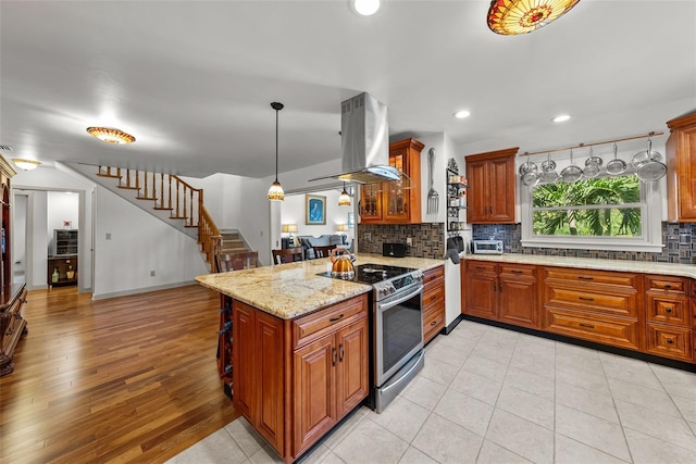 kitchen with stainless steel range, hanging light fixtures, kitchen peninsula, island exhaust hood, and light wood-type flooring