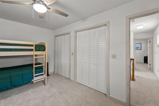 carpeted bedroom with ceiling fan and multiple closets