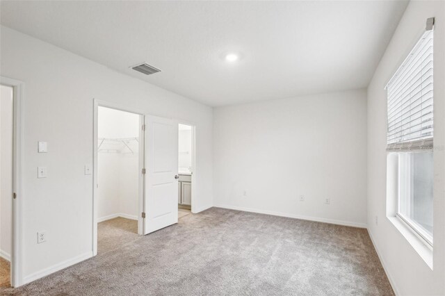 unfurnished bedroom with a walk in closet, light carpet, and a closet