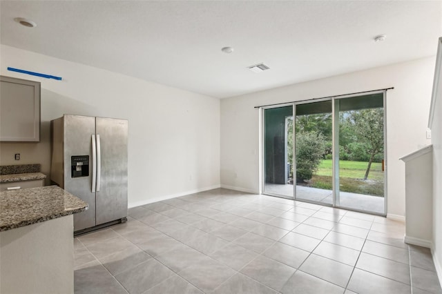 kitchen featuring stainless steel fridge with ice dispenser, gray cabinets, light tile patterned floors, and dark stone countertops