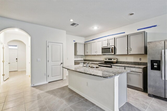 kitchen featuring light stone countertops, stainless steel appliances, gray cabinets, and an island with sink