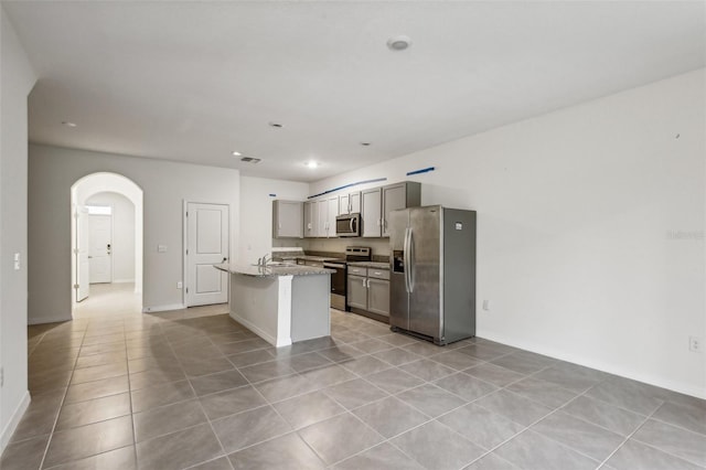 kitchen featuring light stone countertops, appliances with stainless steel finishes, light tile patterned floors, gray cabinets, and an island with sink