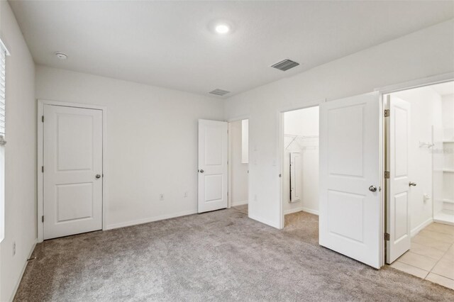 unfurnished bedroom with a spacious closet, light carpet, connected bathroom, and a closet