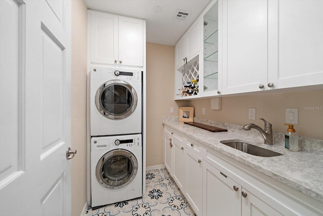 laundry area featuring stacked washing maching and dryer, sink, light tile patterned floors, and cabinets