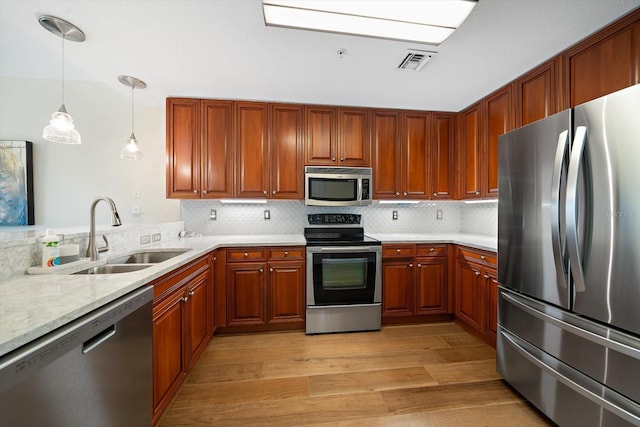 kitchen with sink, stainless steel appliances, backsplash, decorative light fixtures, and light wood-type flooring