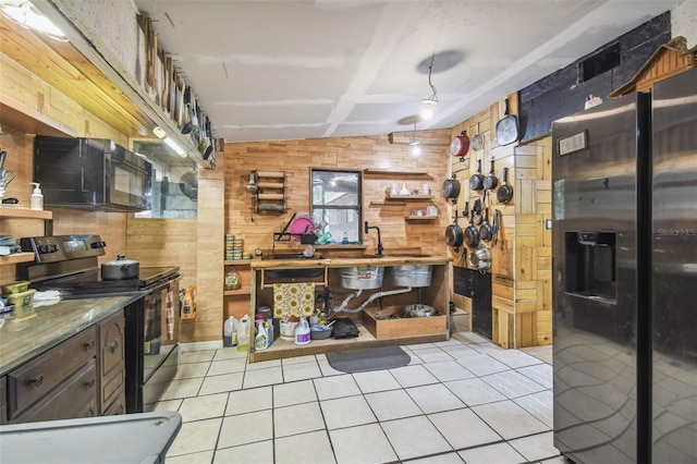 kitchen with a sink, wood walls, black appliances, and light tile patterned floors