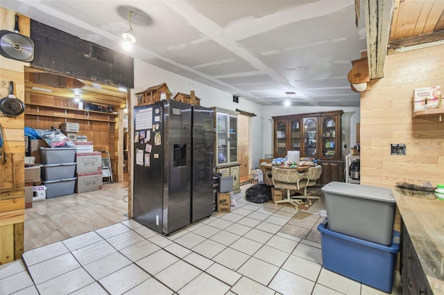 kitchen with light tile patterned floors, wood walls, and stainless steel fridge with ice dispenser