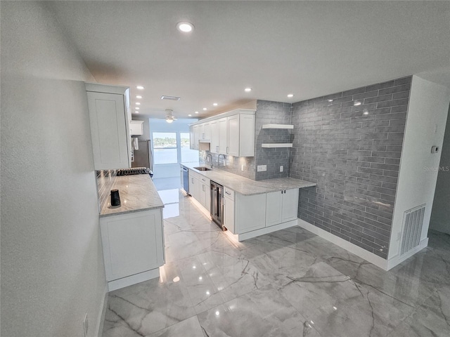 kitchen with sink, white cabinetry, light stone counters, kitchen peninsula, and decorative backsplash