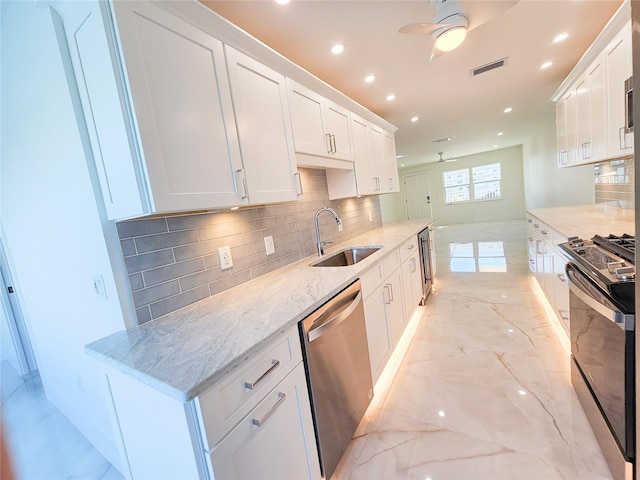 kitchen with sink, ceiling fan, appliances with stainless steel finishes, white cabinetry, and light stone counters