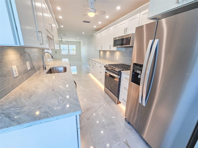 kitchen with white cabinetry, sink, ceiling fan, light stone counters, and stainless steel appliances