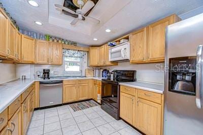 kitchen featuring ceiling fan, a raised ceiling, light brown cabinetry, light tile patterned floors, and appliances with stainless steel finishes