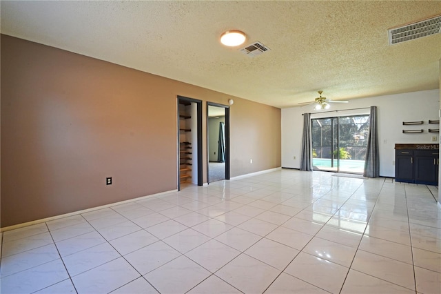 tiled empty room with ceiling fan and a textured ceiling