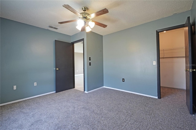 unfurnished bedroom with ceiling fan, a spacious closet, a textured ceiling, carpet floors, and a closet