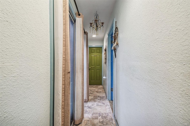 15577 Little Ranch Rd, Spring Hill, FL 34610 - corridor featuring a textured wall, stone finish flooring, and a chandelier