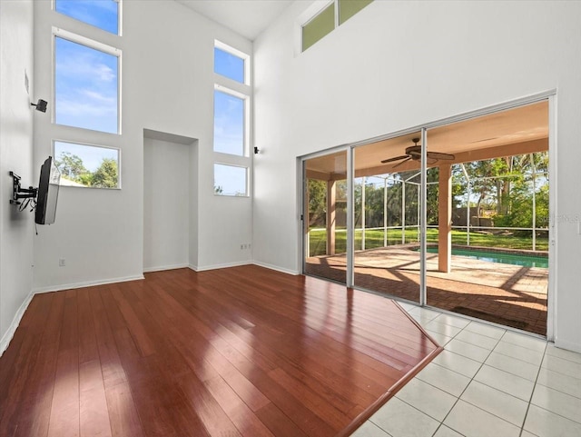 unfurnished living room with ceiling fan, light hardwood / wood-style floors, a healthy amount of sunlight, and a high ceiling