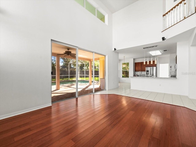 unfurnished living room with ceiling fan, light hardwood / wood-style flooring, and a towering ceiling