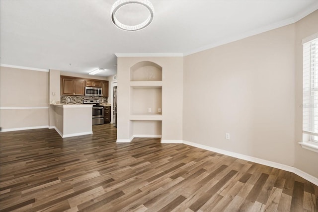 unfurnished living room with built in shelves, dark hardwood / wood-style flooring, a wealth of natural light, and crown molding