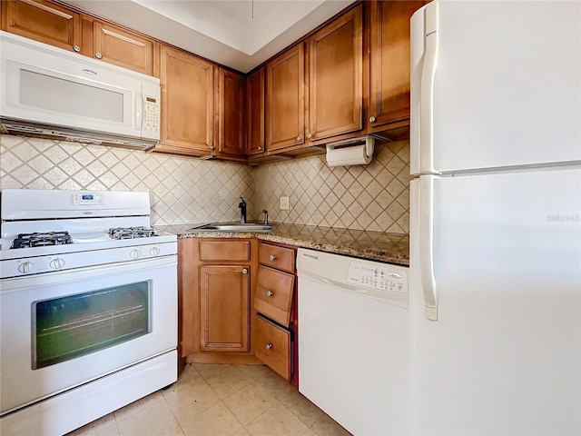 kitchen with backsplash, light stone counters, sink, and white appliances