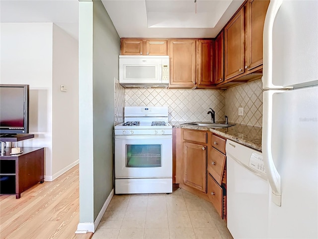 kitchen featuring decorative backsplash, light stone countertops, light wood-type flooring, white appliances, and sink