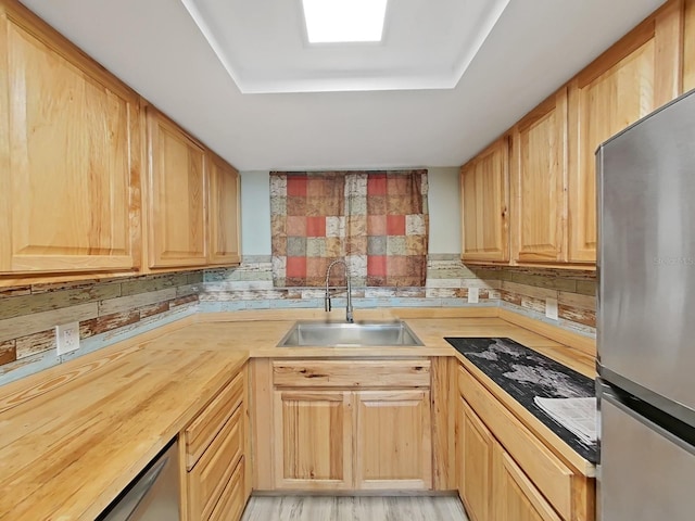 kitchen featuring light brown cabinets, a skylight, a sink, appliances with stainless steel finishes, and a raised ceiling