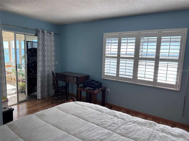 bedroom with multiple windows, hardwood / wood-style floors, a water view, and a textured ceiling