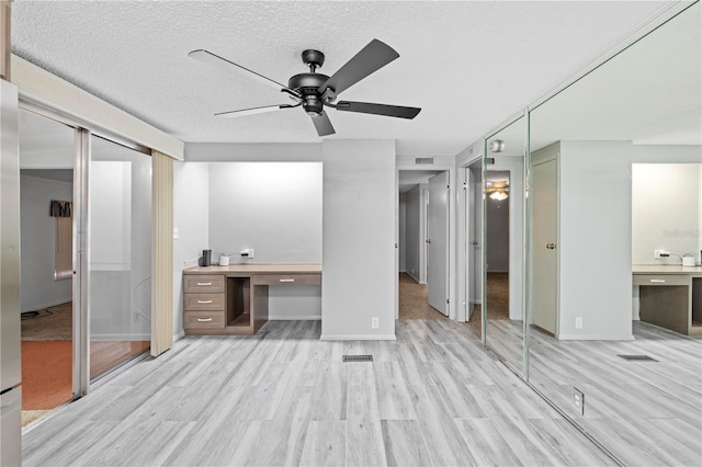 unfurnished bedroom featuring ensuite bath, a textured ceiling, ceiling fan, built in desk, and light hardwood / wood-style floors