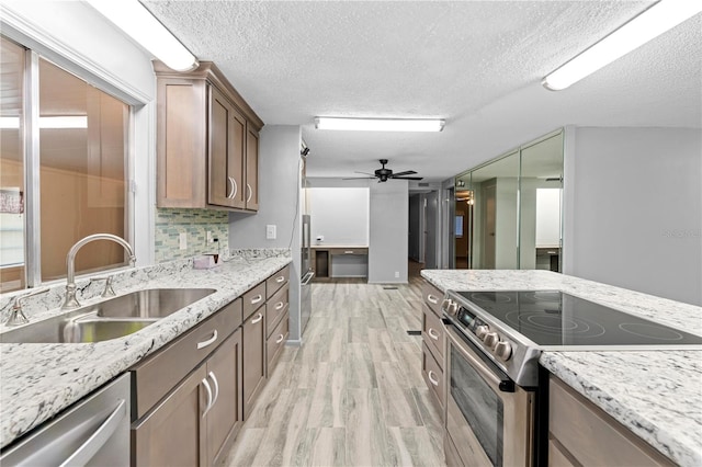 kitchen with appliances with stainless steel finishes, a textured ceiling, ceiling fan, sink, and light hardwood / wood-style flooring